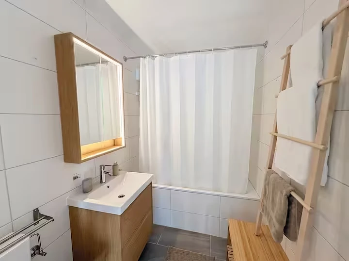 Salle de bain avec meuble vasque en bois, miroir éclairé, baignoire et porte-serviettes échelle