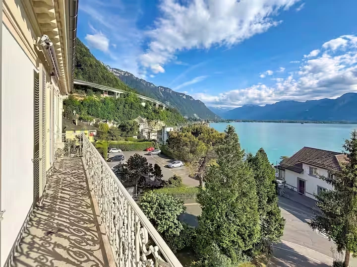 Balcon en fer forgé surplombant les arbres, avec vue sur le lac et les montagnes