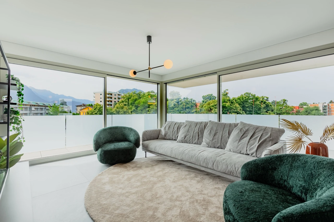 Salon lumineux entièrement vitré, canapé gris et fauteuils en velours vert
